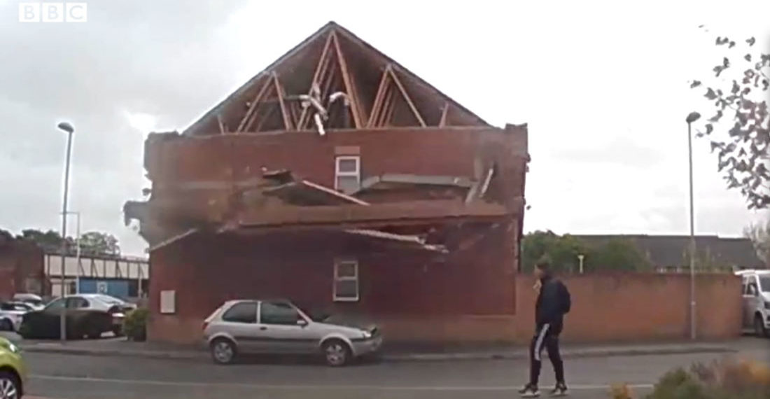 Man Casually Walks By Building As Wall Partially Collapses Right In Front Of Him