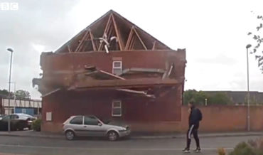 Man Casually Walks By Building As Wall Partially Collapses Right In Front Of Him
