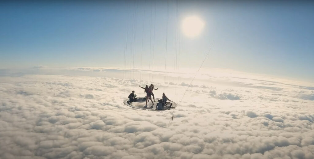 Jumping On A Trampoline Suspended Below A Hot Air Balloon Above The Clouds